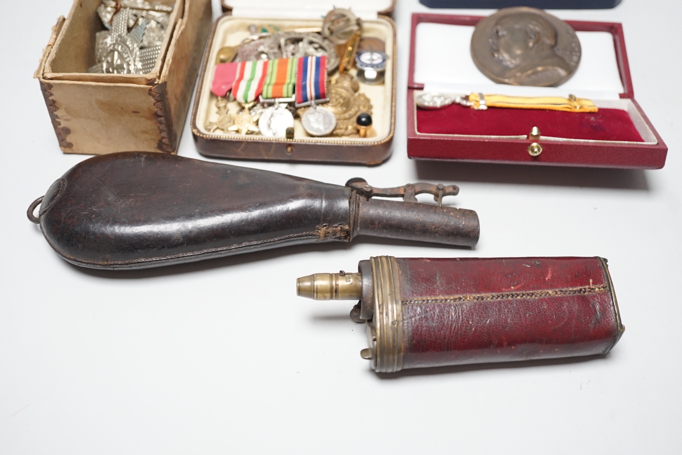 Two powder flasks and militaria including cap badges and miniature medals